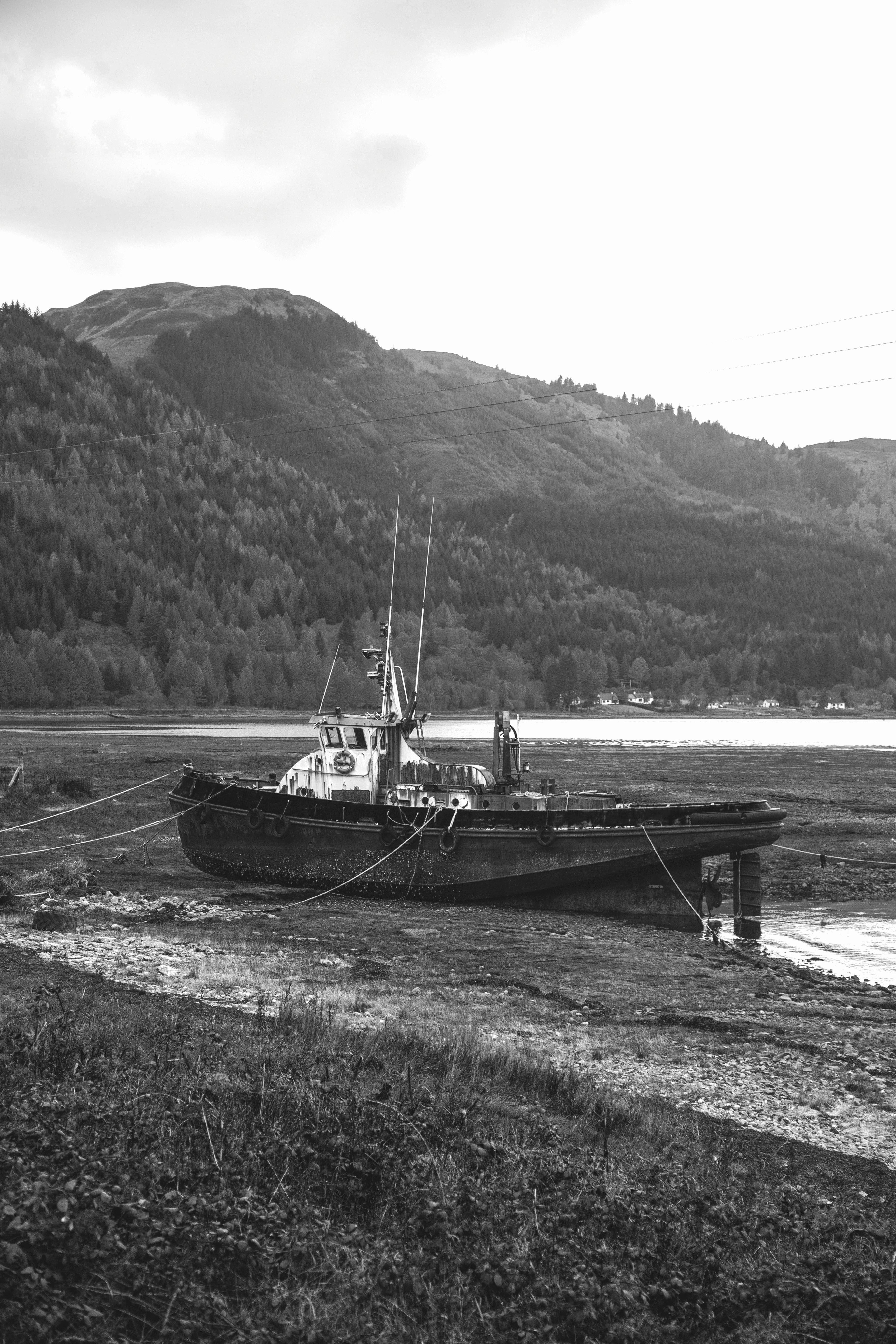grayscale photo of boat on sea near mountain